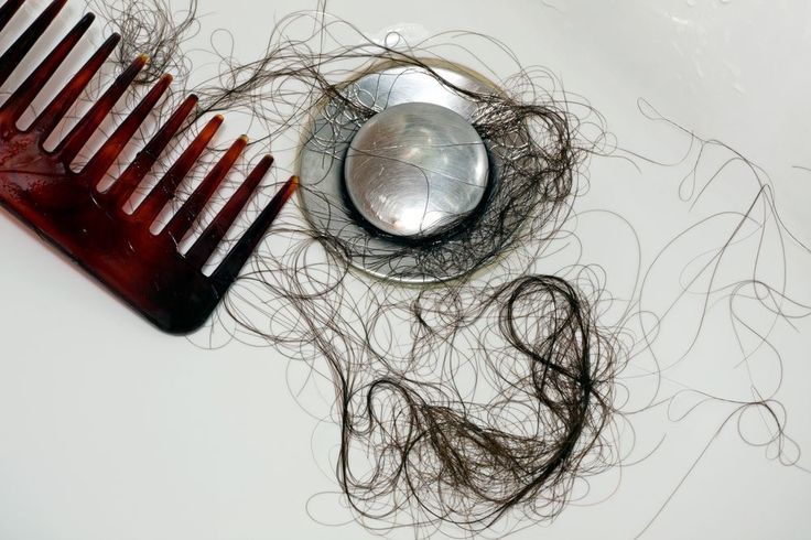 A hair comb and a clump of dark hair wrapped around the bath plug hole