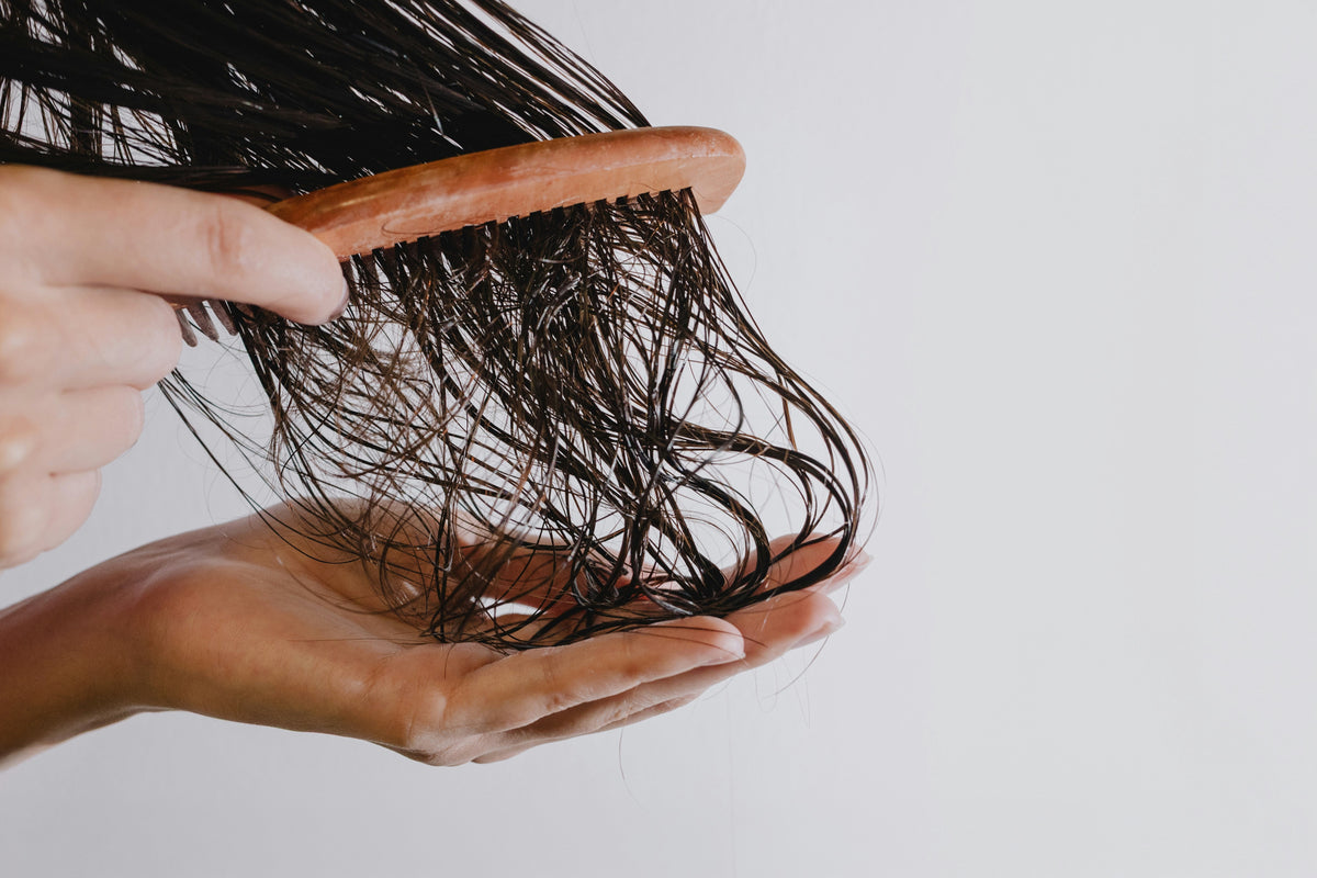 Woman detangling long wet brown hair with a wooden comb after washing