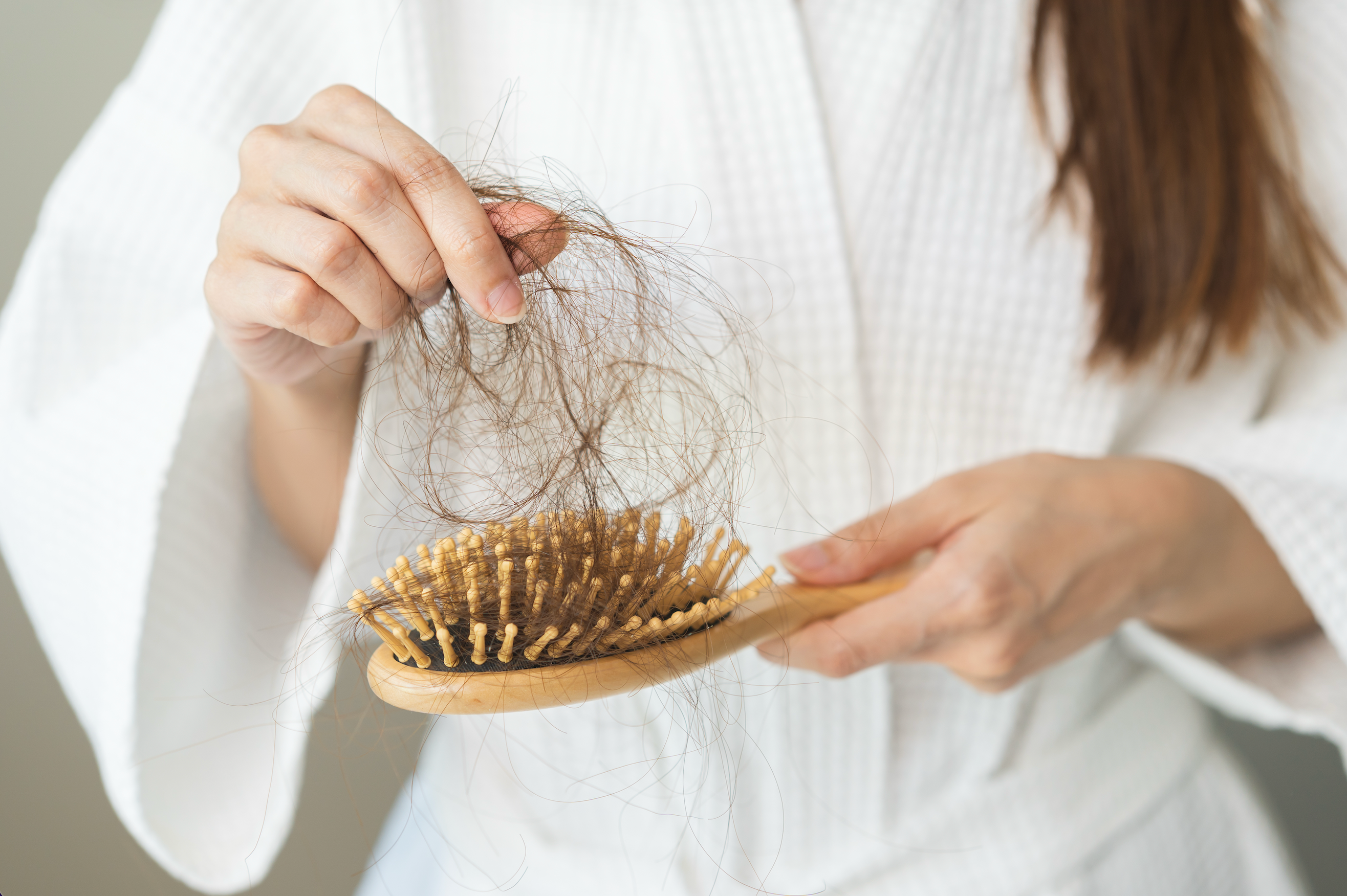 Close up of a woman wearing a white robe pulling a clump of hair from a hair brush