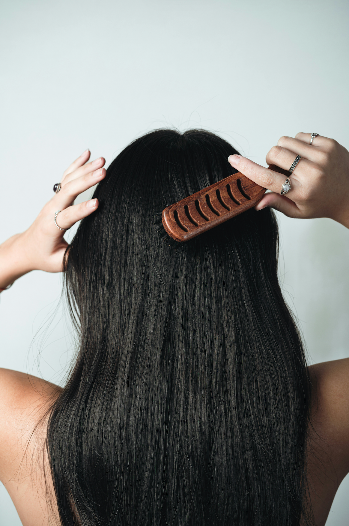 Woman brushing long black hair with wooden brush from behind