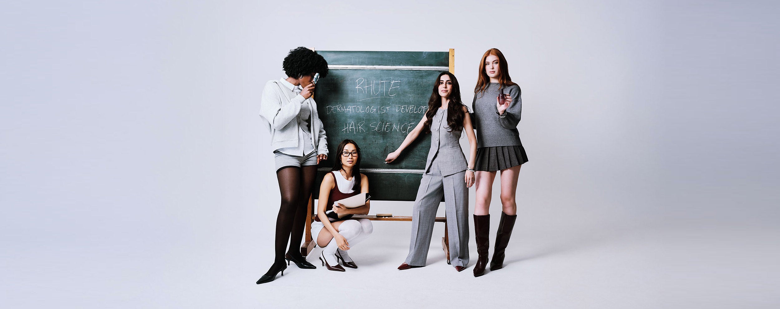 Four women in formal attire standing in front of a chalkboard with text on a white background