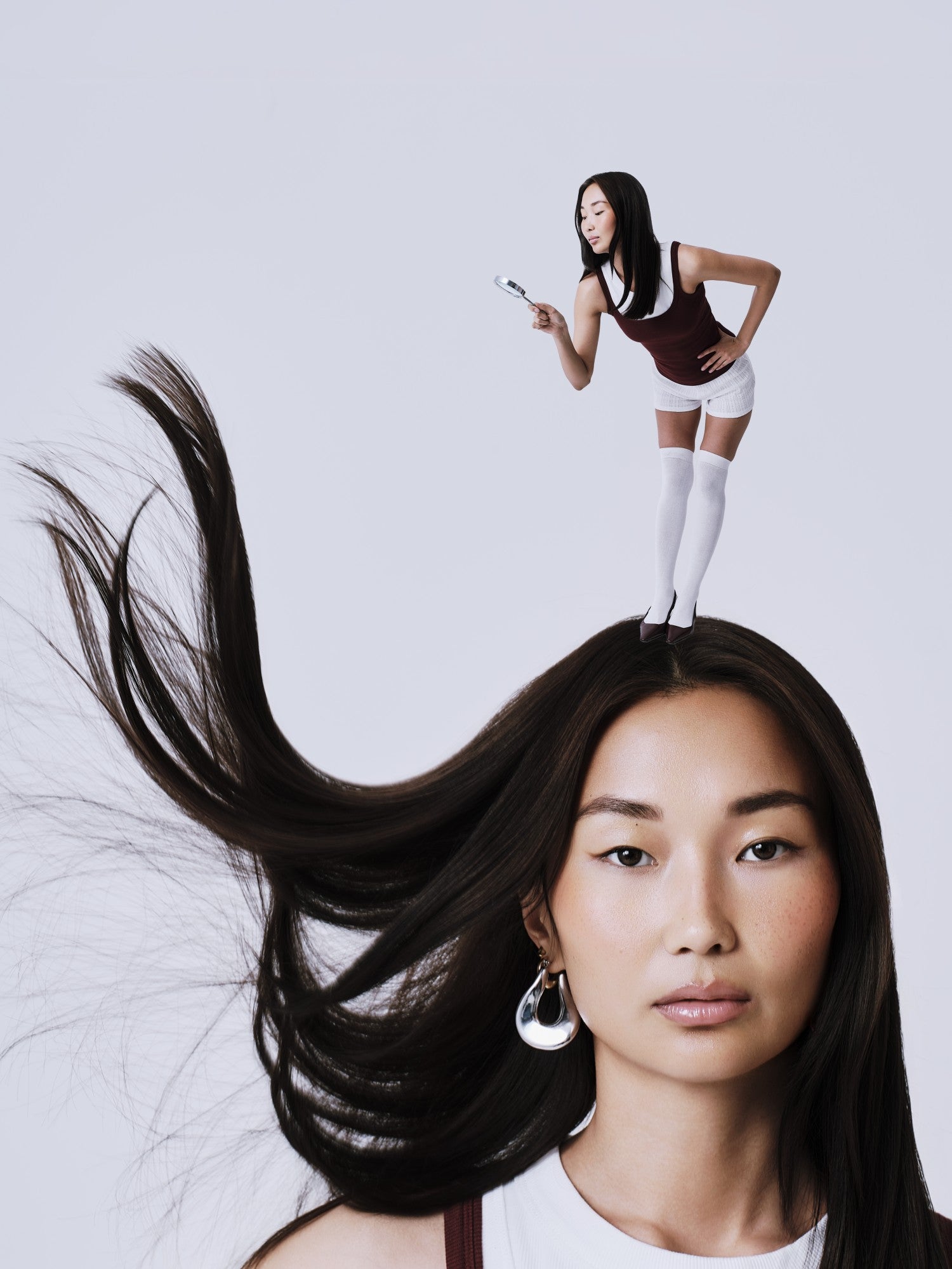 Woman with long hair and another woman standing on top of it against a light gray background