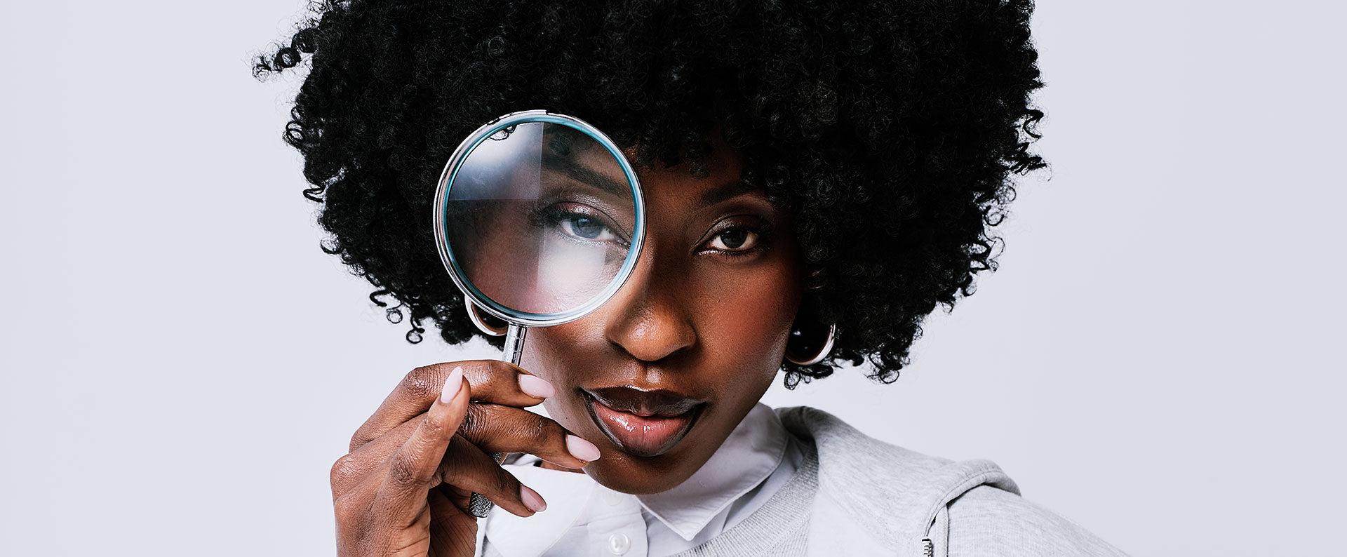 Person holding a magnifying glass to their eye against a plain background