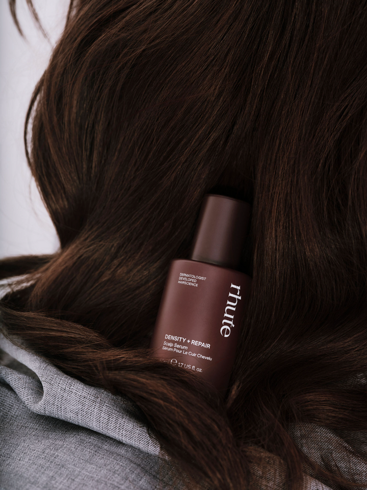bottle of rhute product nestled in dark hair with a blurred background