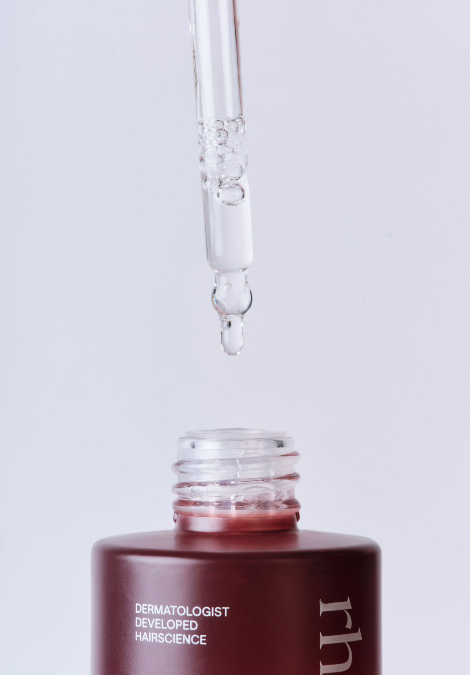 Bottle of dermatologist-developed hairscience with dropper on a light gray background