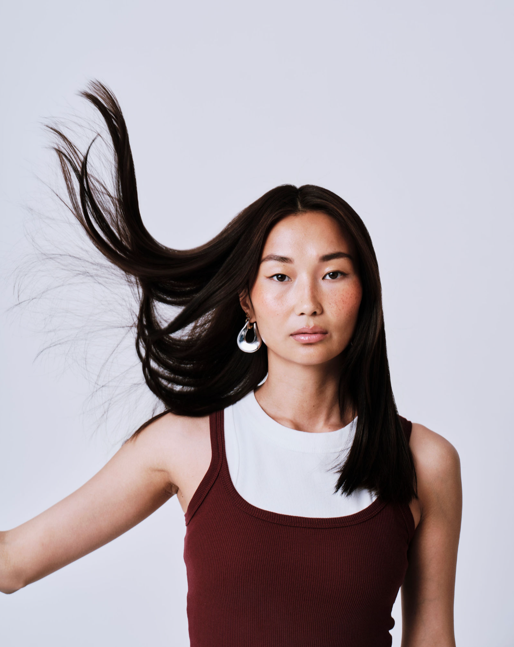 rhute girl with long, dark hair blowing in the wind against a plain background