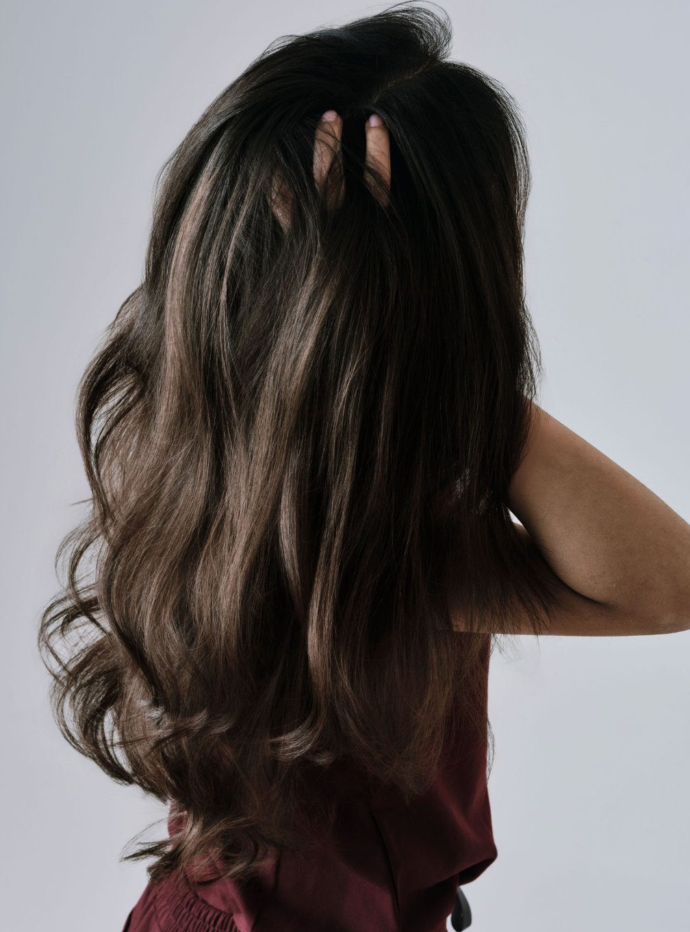 Person with long, wavy hair touching their head against a plain background
