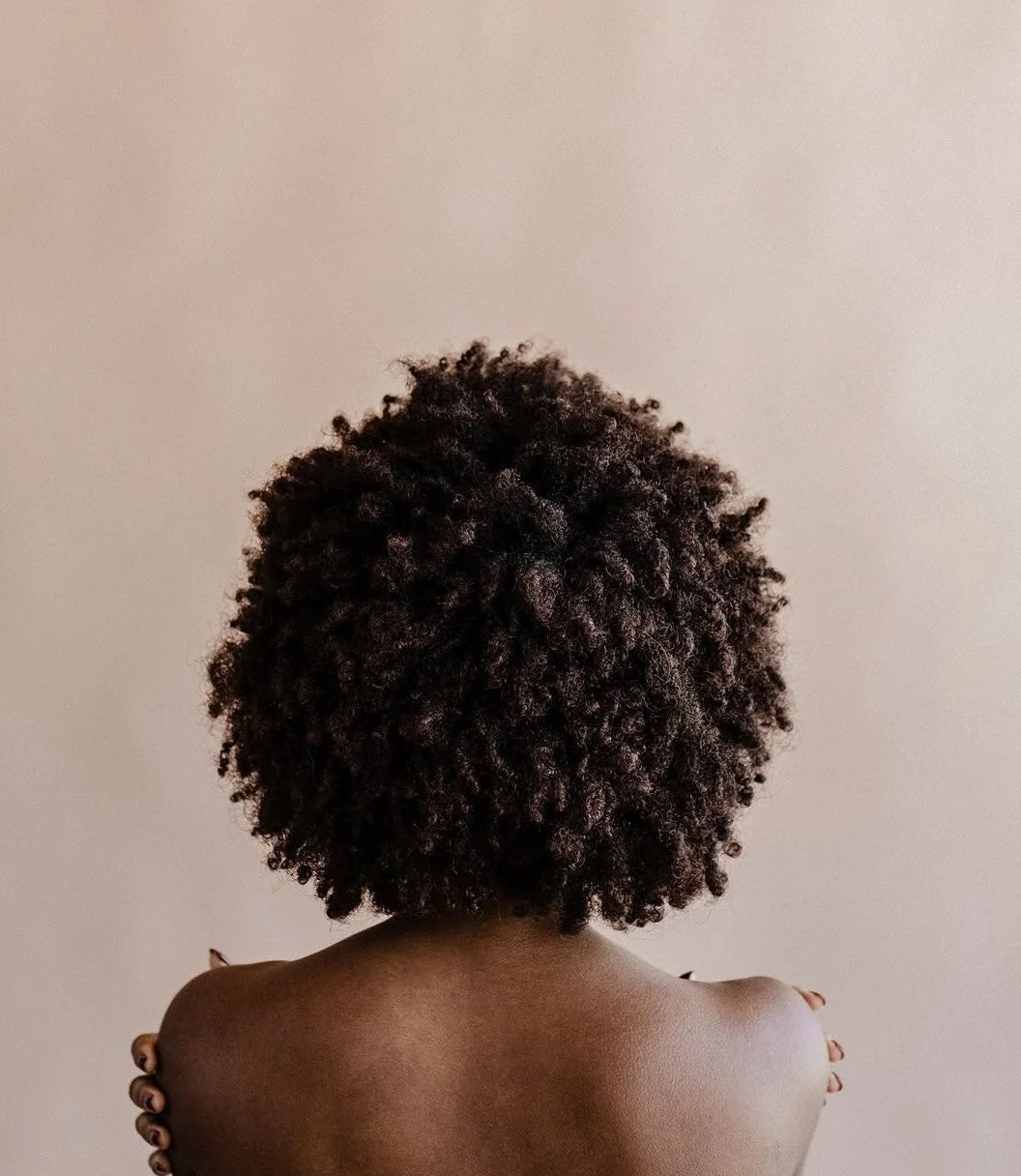 Black woman with healthy hair from behind with hands cupping shoulders