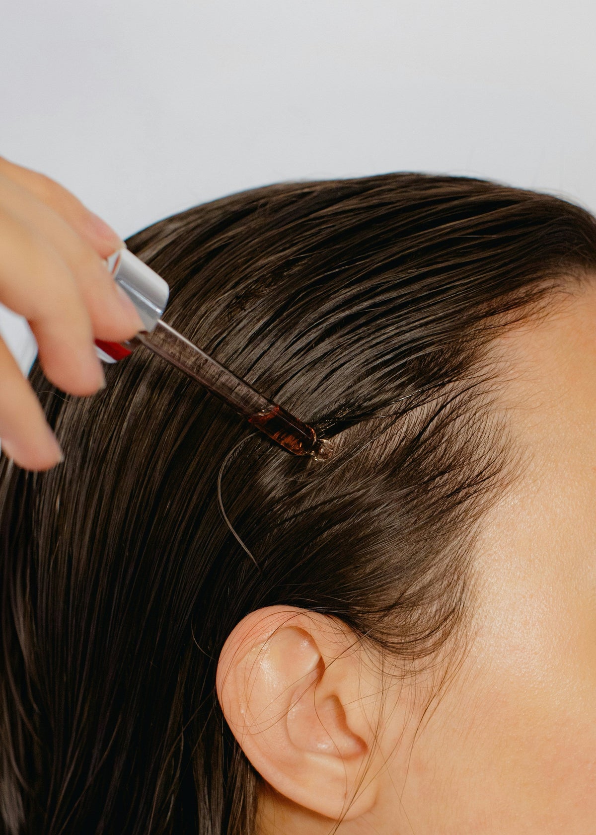 Side profile close up of woman applying hair oil drops close up
