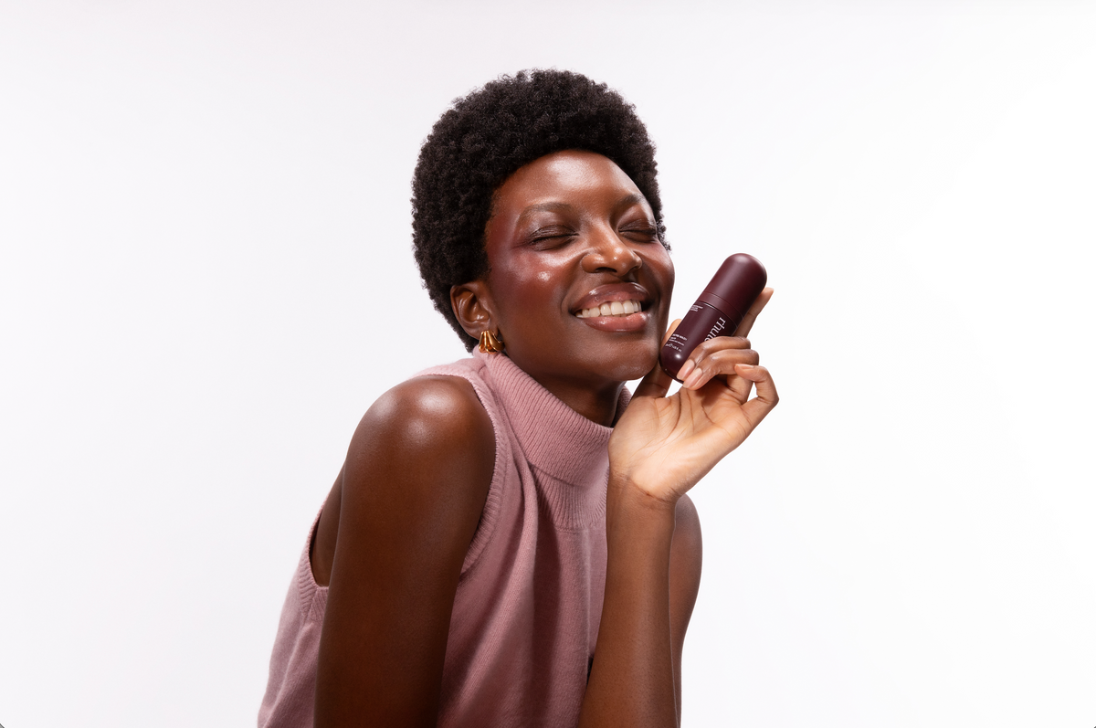 Smiling woman with a short natural afro holding a bottle of Rhute Pre-Wash Hair Oil against her cheek