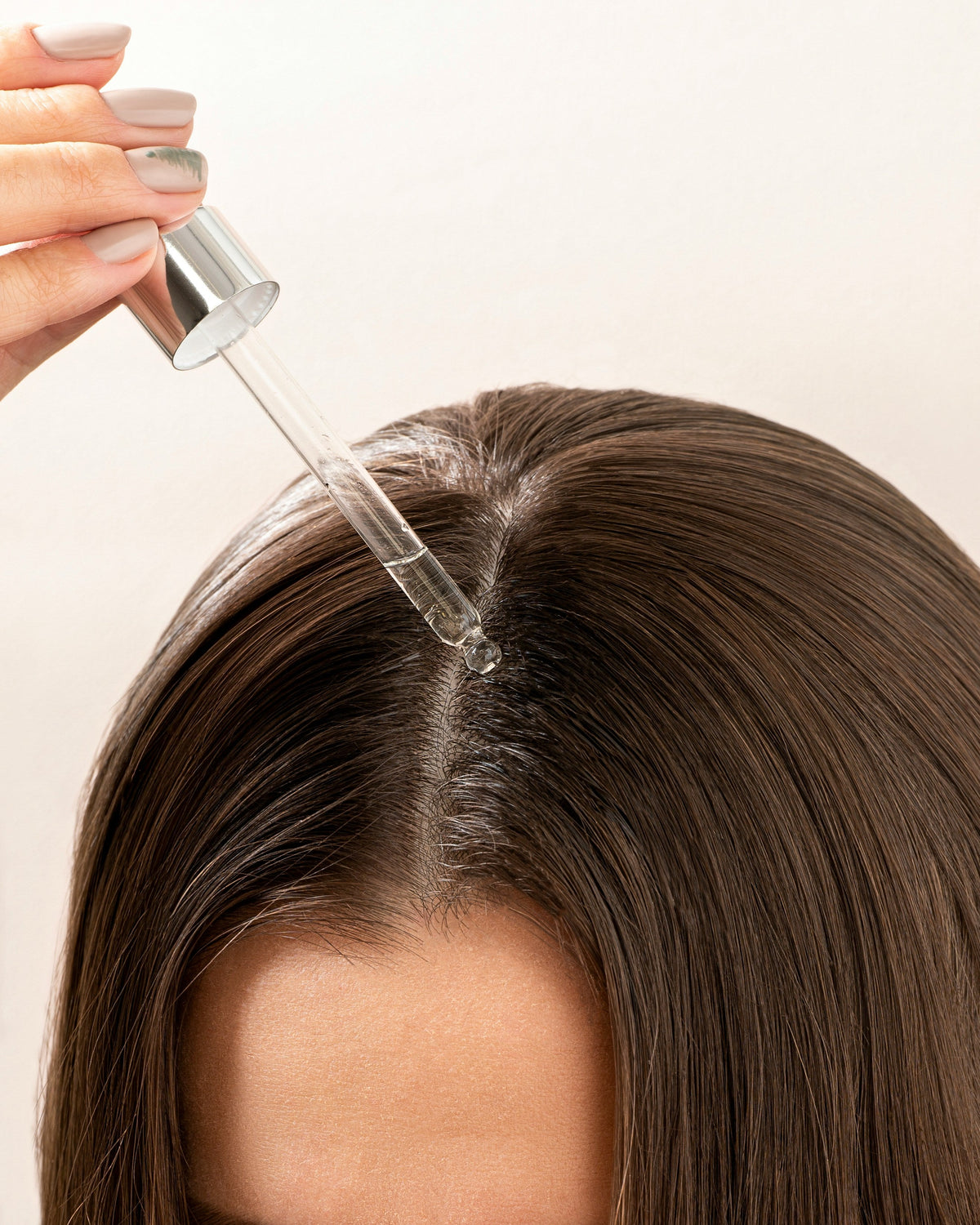 Woman with dark brown hair applying hair oil to scalp close up