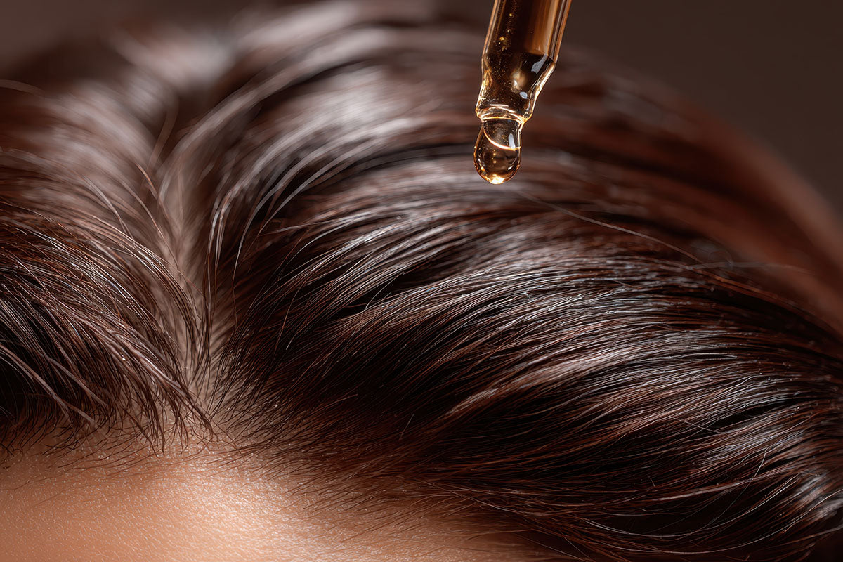Close up of serum dropping onto top of woman's scalp with dark brown hair