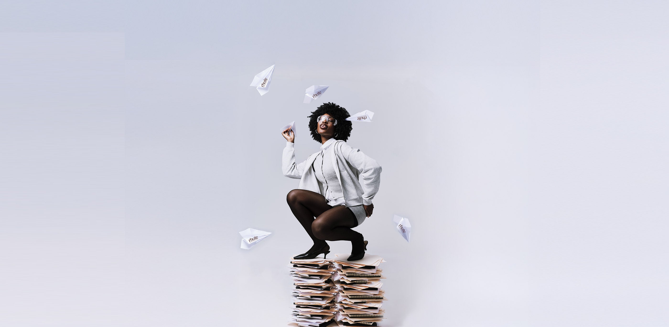Woman sitting on a stack of books with papers flying around her against a light gray background