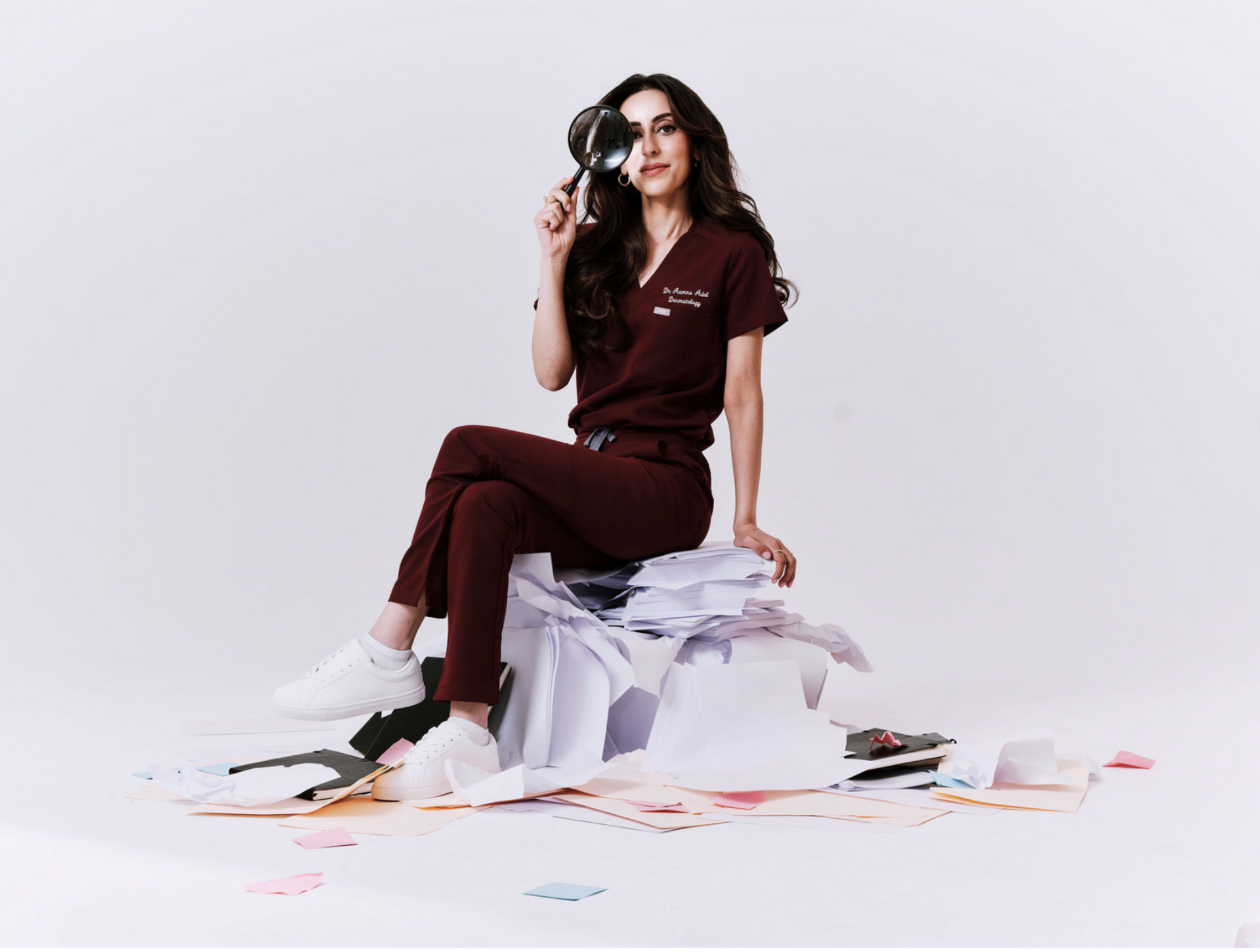 Dr Aamna in brown outfit sitting on a pile of papers with a mirror.