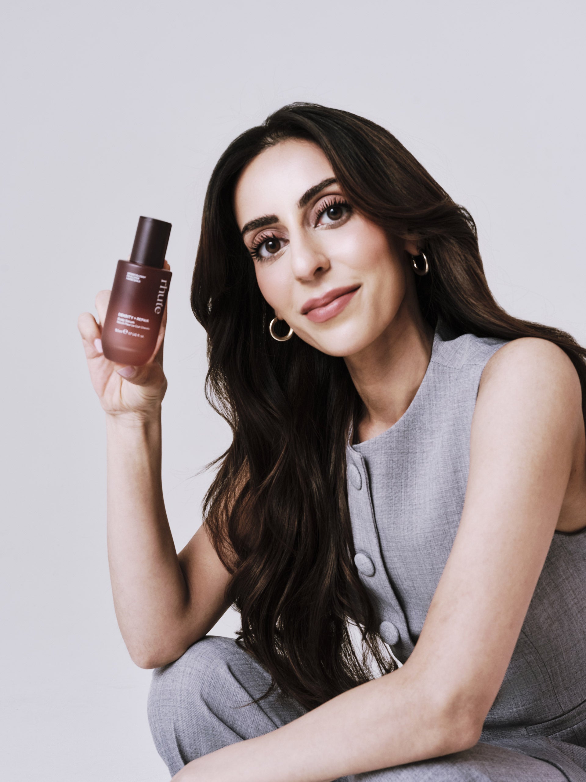 Woman holding a bottle of hair serum product against a plain background