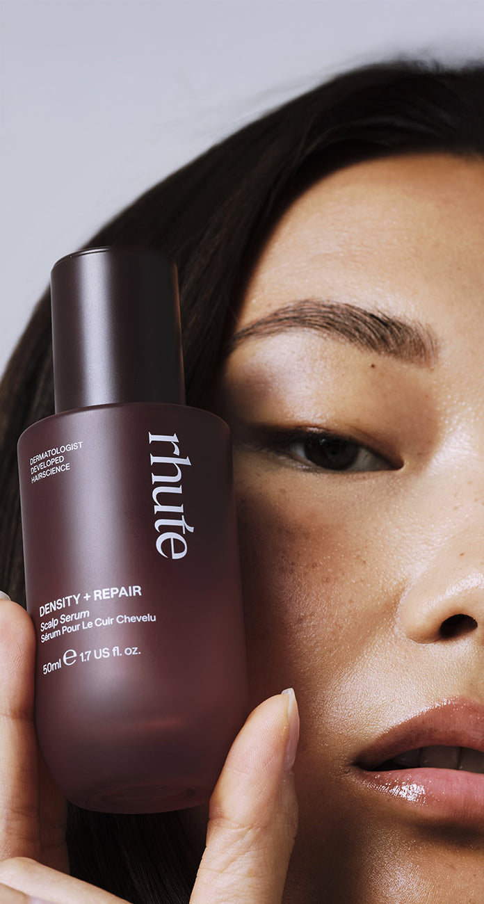 Close-up of a model holding a Rhute ‘Density + Repair’ Scalp Serum bottle beside their face.