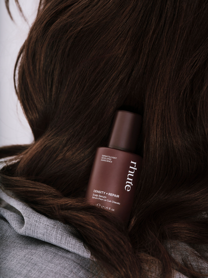 bottle of rhute product nestled in dark hair with a blurred background

